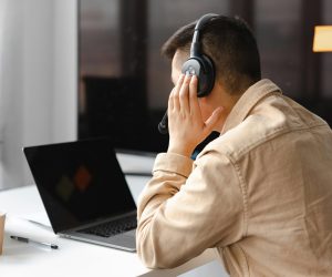 A man wearing headphones works at a laptop in a modern office setting.
