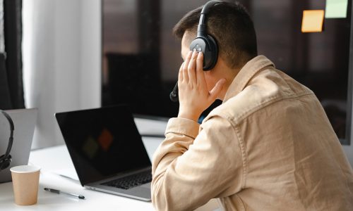 pexels-photo-7681302-7681302 A man wearing headphones works at a laptop in a modern office setting.